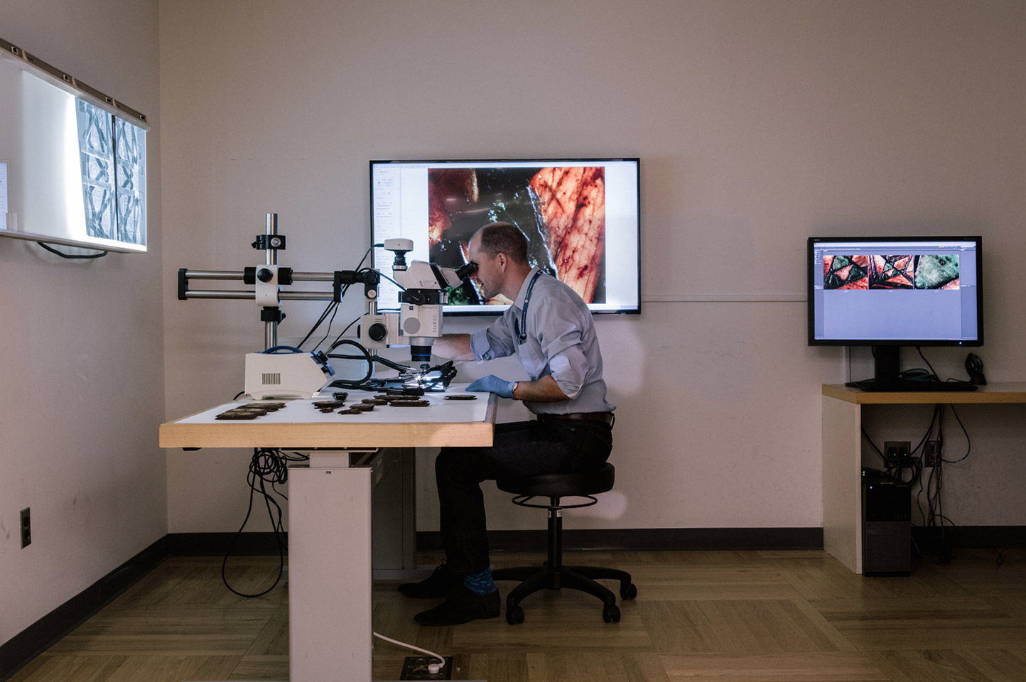 Man looking through a microscope surrounded by screens
